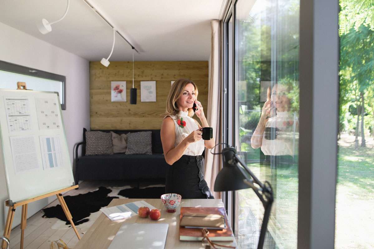 Frau telefoniert in einem modernen Luxus-Gartenhaus-Container und schaut aus dem Fenster